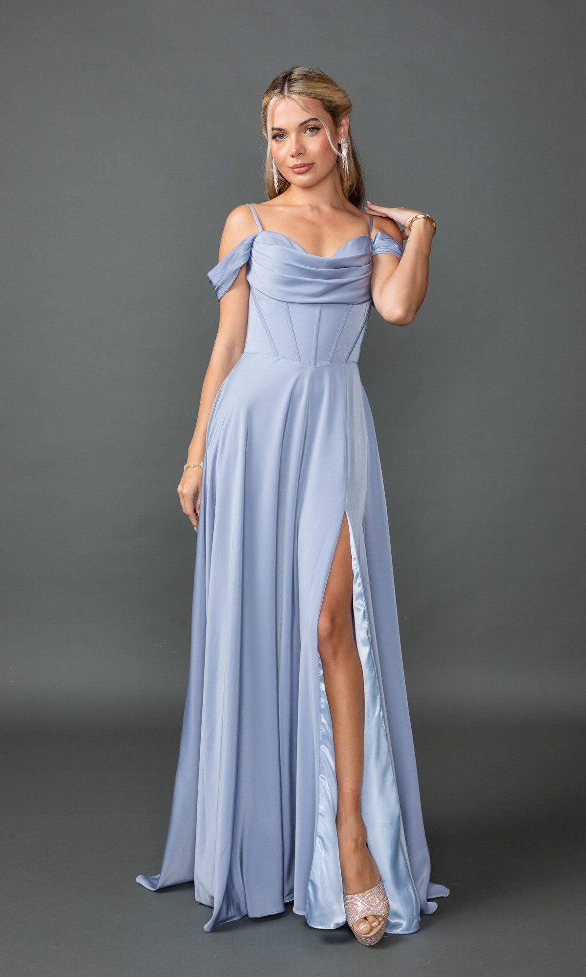 A woman wearing the Long Prom Dress: Dancing Queen 4539, featuring a light blue A-line silhouette, corset bodice, and dramatic leg slit, stands against a plain gray background.